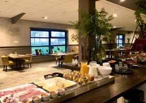 Zona de buffet con diversos alimentos y un ventanal con vistas a árboles.