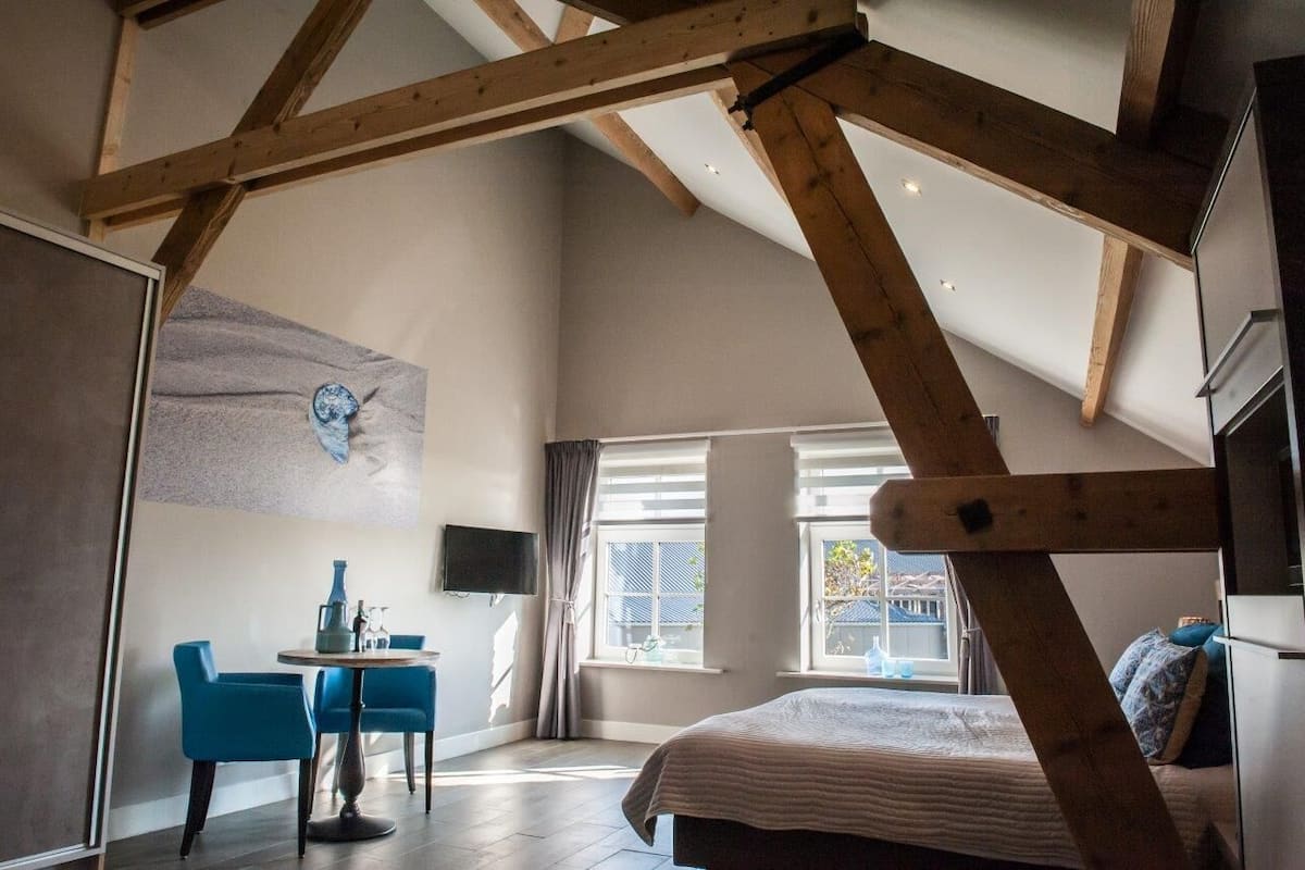 A bedroom with a sloped ceiling, a bed, a desk with chairs, and a window with curtains.