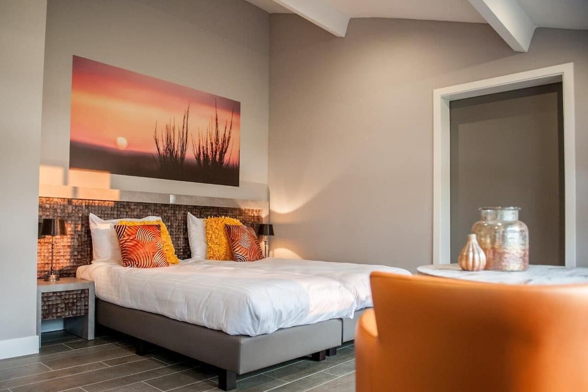 A bedroom with a bed, a nightstand, a table with jars, and a painting on the wall.