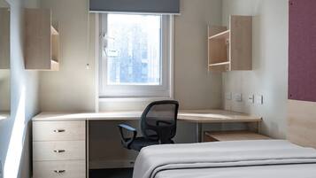 A bedroom with a single bed, a desk with a chair, a window, and built-in shelving.