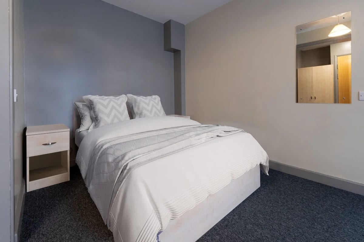 Una camera da letto con un letto, un comodino, uno specchio e un pavimento rivestito di moquette.