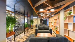 A modern lounge area with a herringbone patterned floor, grey sofas, wooden shelving with plants, and a wooden coffee table. - For Students Only Canvas The Heights in Birmingham (Birmingham)