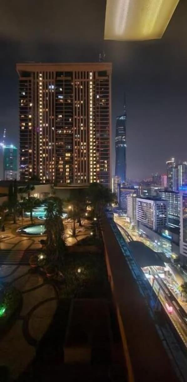A nighttime cityscape with a prominent skyscraper, a well-lit building with multiple floors, and a landscaped area with a pool.
