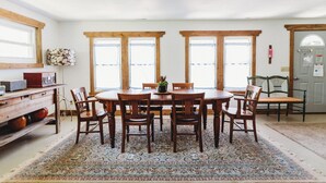 A dining area with a wooden table and chairs, surrounded by large windows. - Cozy Nook by Lake MI&Dunes with Private Hot Tub! (Harbert)