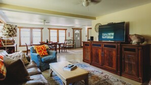 A spacious living room with a large television, wooden cabinets, and a blue sofa. - Cozy Nook by Lake MI&Dunes with Private Hot Tub! (Harbert)