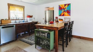A kitchen with a wooden table, chairs, a refrigerator, a microwave, and a colorful geometric wall art. - Cozy Nook by Lake MI&Dunes with Private Hot Tub! (Harbert)