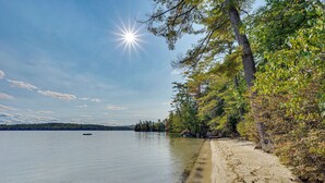 Un lago tranquillo con una barca, circondato da alberi e una spiaggia sabbiosa.