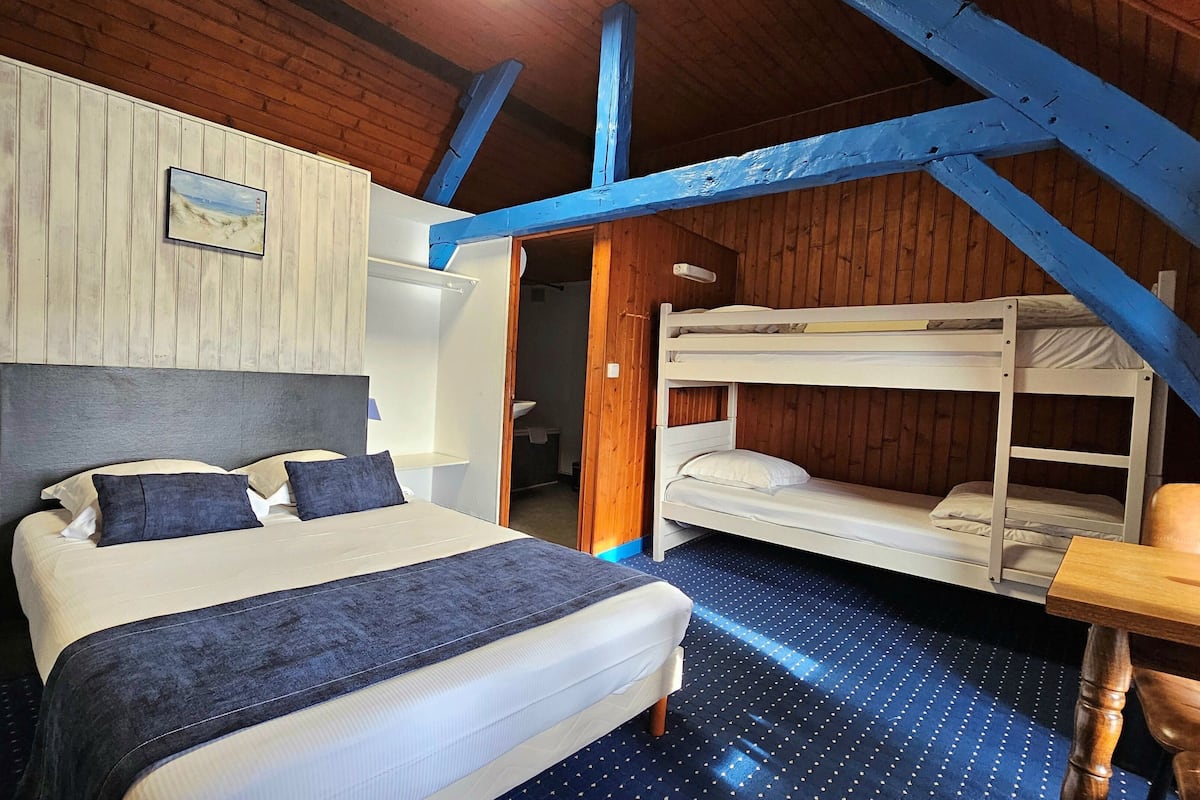 A bedroom with a large bed, a bunk bed, wooden walls, and a blue ceiling beam.