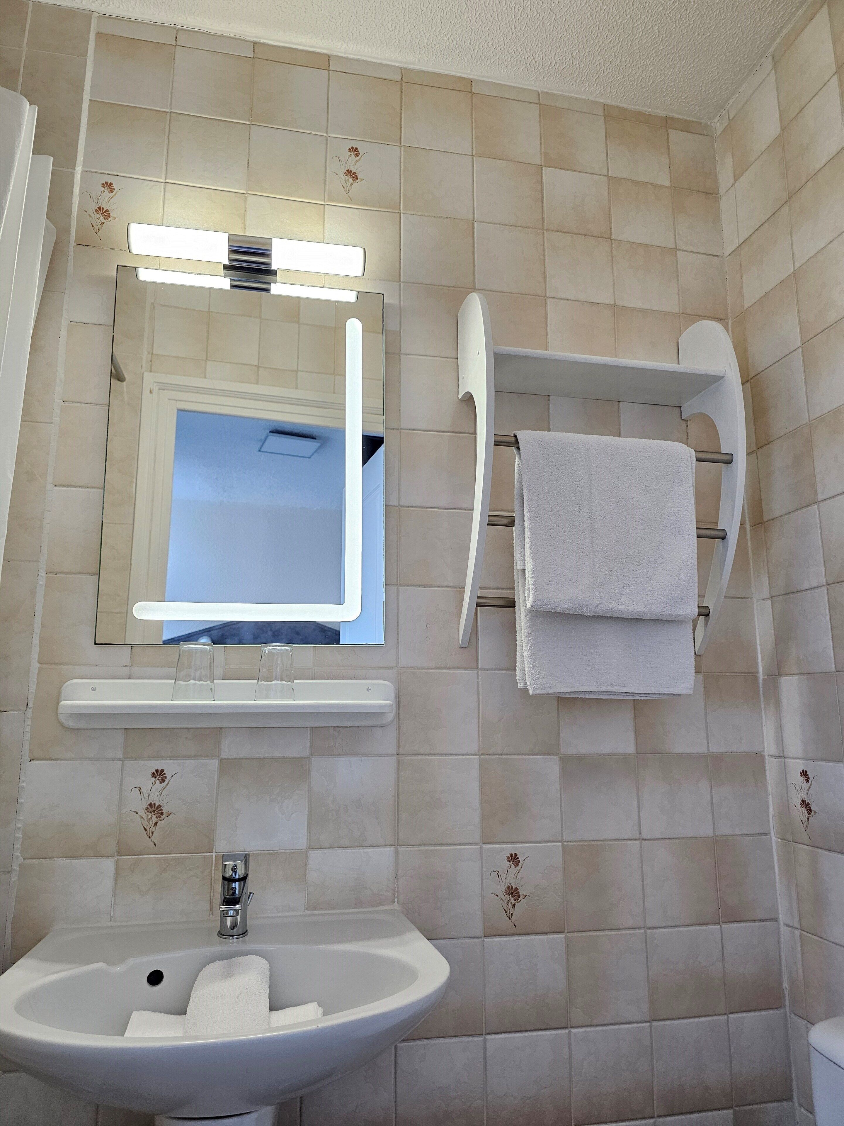 Une salle de bain avec un lavabo, un miroir, un porte-serviettes et des murs carrelés.