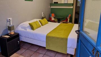 A hotel room with a bed, a nightstand, a table with chairs, a green wall, and a door with a number.