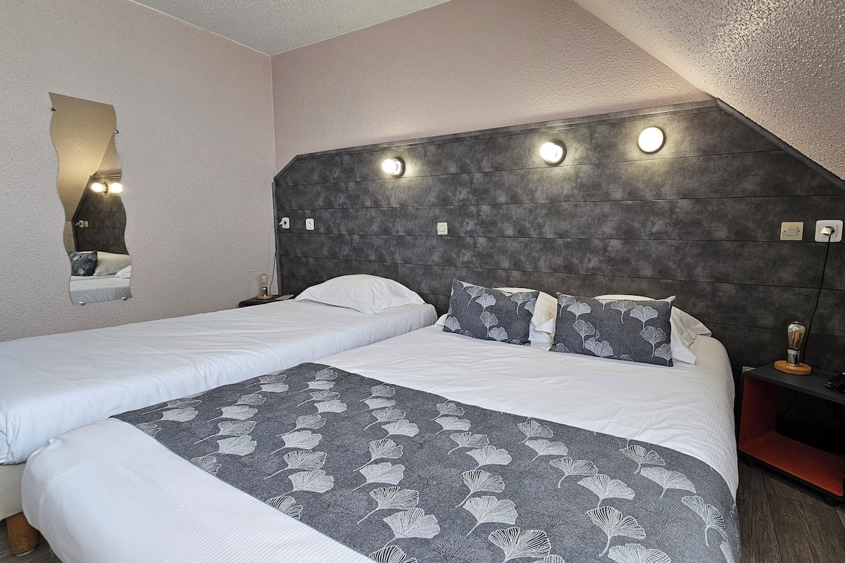 A double room with two beds, a headboard with integrated lighting, a bedside table with a phone, and a mirror on the wall.