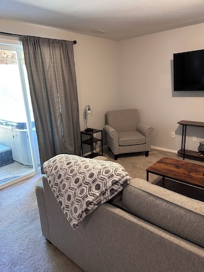 Una sala de estar con sofá, una mesa de centro, una silla, televisor y ventana con cortinas.