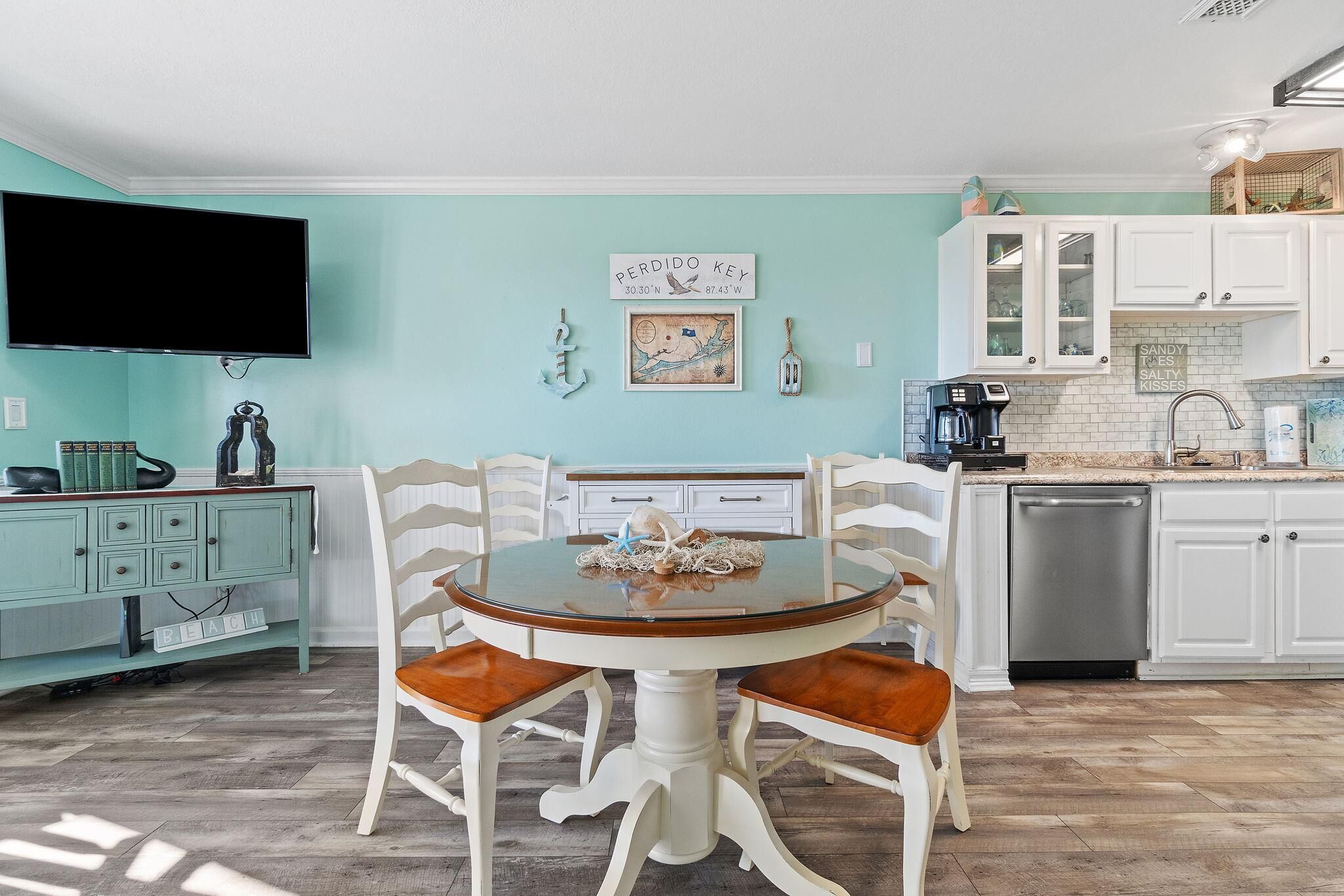 Une cuisine avec une table ronde, des meubles blancs et un téléviseur fixé au mur.