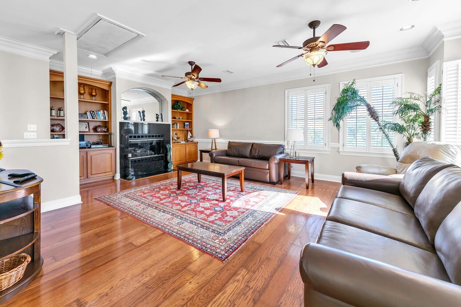 A spacious living room with hardwood floors, a fireplace, a large sofa, a coffee table, and a ceiling fan.