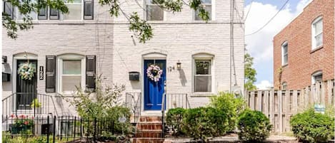 A two-story building with a blue front door, a brick entrance, and a small front garden.