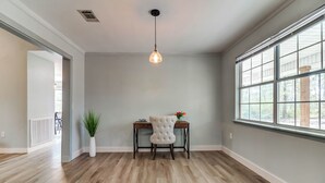 A spacious room with hardwood flooring, a tufted chair, a desk, and a hanging light fixture.