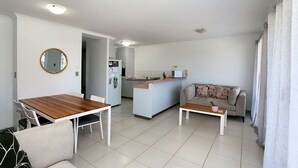 A compact living space with a dining table, a sofa, a coffee table, and a kitchen area. - Capricorn Pacific - 2 Bedroom, 2 bathroom apartment with Ocean views (Bargara)