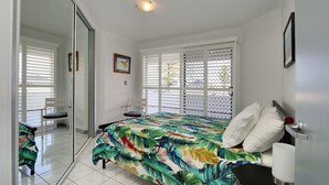 A bedroom with a bed, a chair, a bedside table, and a window with blinds. - Capricorn Pacific - 2 Bedroom, 2 bathroom apartment with Ocean views (Bargara)