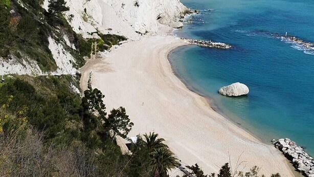 A coastal landscape with a sandy beach, clear blue sea, and a white cliff.