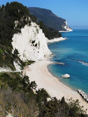 A coastal landscape with a sandy beach, clear blue sea, and a white cliff.