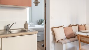 Una cocina moderna con encimera de madera, un lavamanos y un armario blanco. Hay un comedor con mesa y sillas, y un sofá blanco con un arco decorativo al fondo.