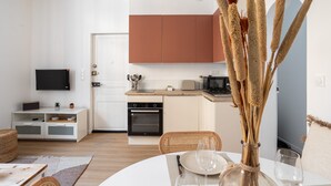 Una cocina moderna con armarios blancos, un microondas y un tostador. Hay una mesa de comedor con un florero de plantas secas.