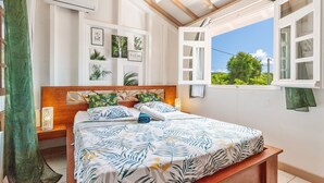 A bedroom with a bed, a wooden headboard, a window with an open shutter, and wall-mounted air conditioning.