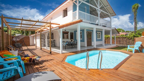 A two-story house with a wooden deck, a swimming pool, and outdoor furniture.