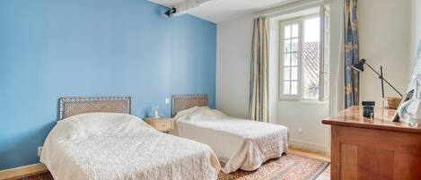 Una habitación con dos camas, un aparador de madera, una ventana con cortinas y una alfombra estampada.