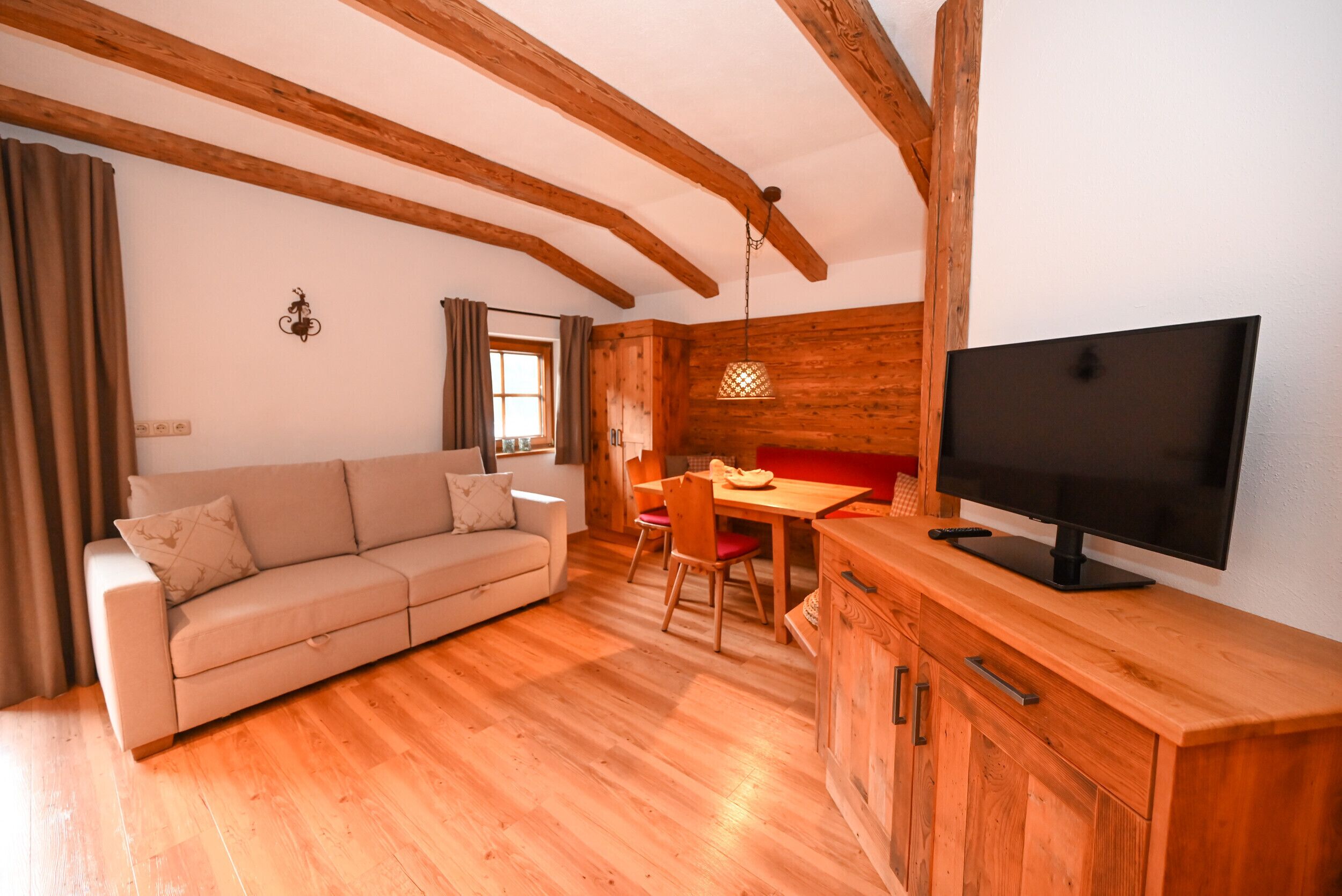 A cozy living room with a sofa, wooden dining table, and a TV on a wooden cabinet.