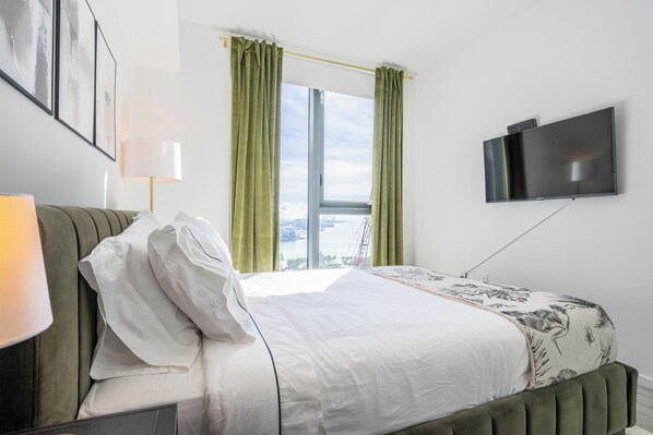 A hotel room with a bed, a TV mounted on the wall, and a window with curtains.