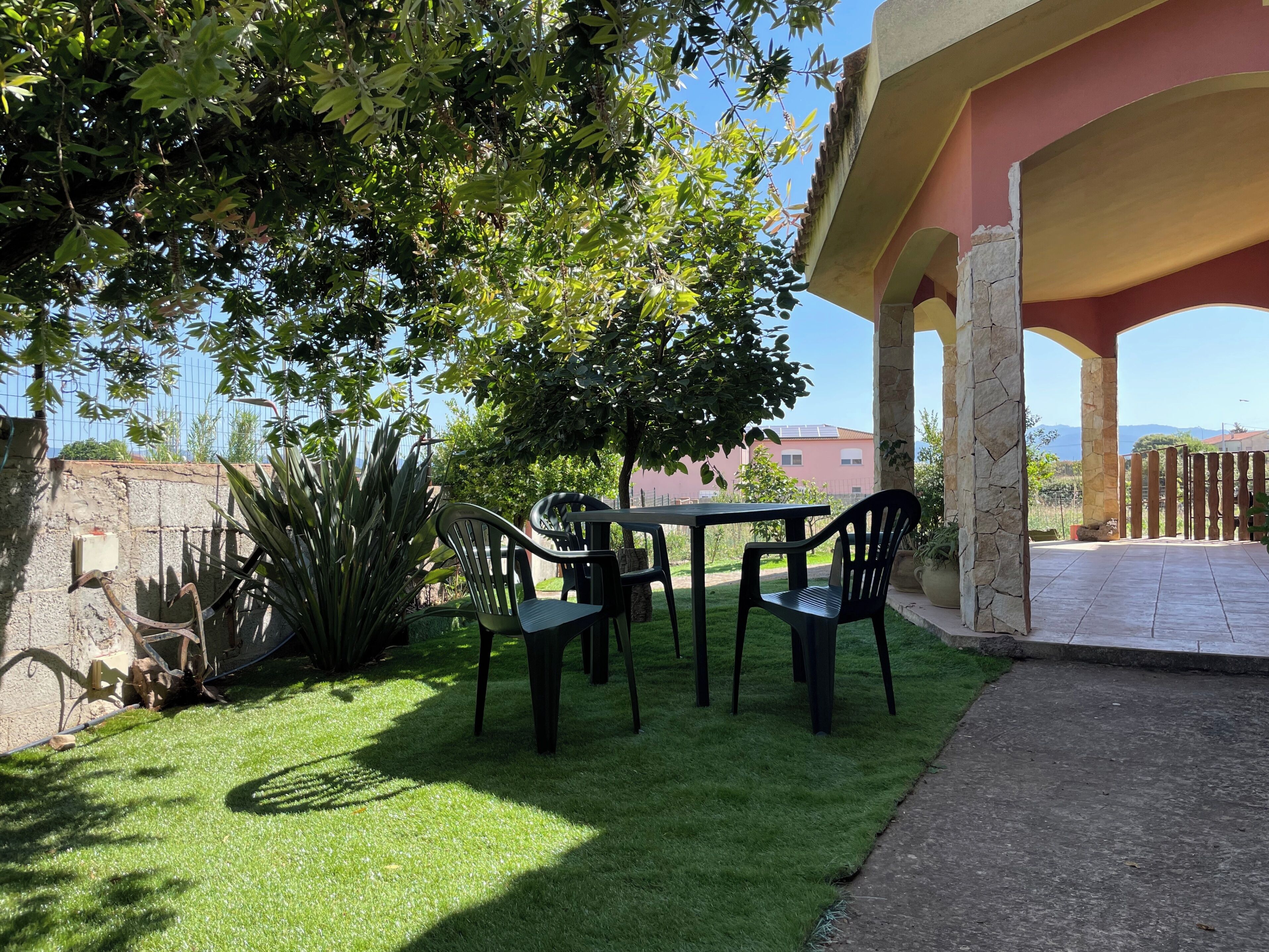 An outdoor patio with a table and chairs, surrounded by greenery and a stone wall.