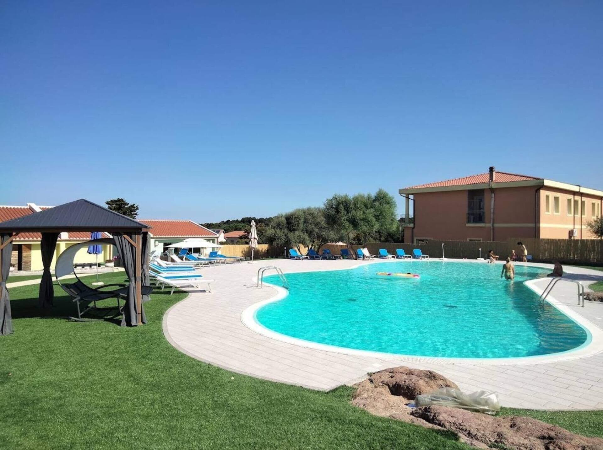 A swimming pool with a curved edge, surrounded by lounge chairs and a covered seating area.