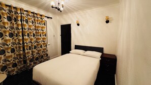A bedroom with a bed, a nightstand, a door, and a curtain with a floral pattern.