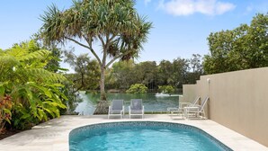 A swimming pool with lounge chairs, surrounded by lush greenery and a view of a lake.