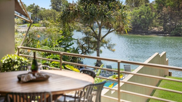 A balcony with a view of a lake, surrounded by greenery and a building in the background.