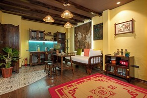 Quarto aconchegante com sofá de madeira, mesa de jantar, área de cozinha e um tapete grande.