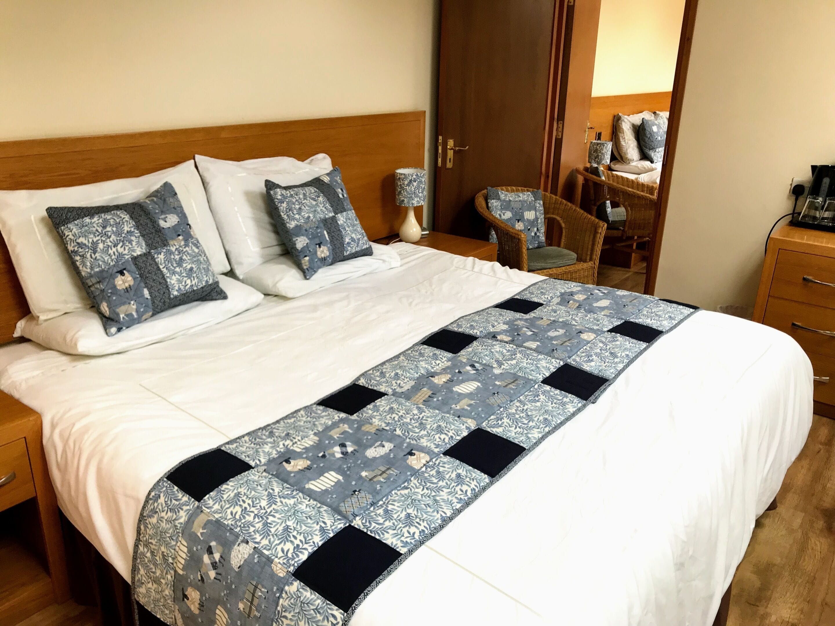 Cama bem arrumada com colcha azul e branca, duas almofadas brancas e cabeceira de madeira.