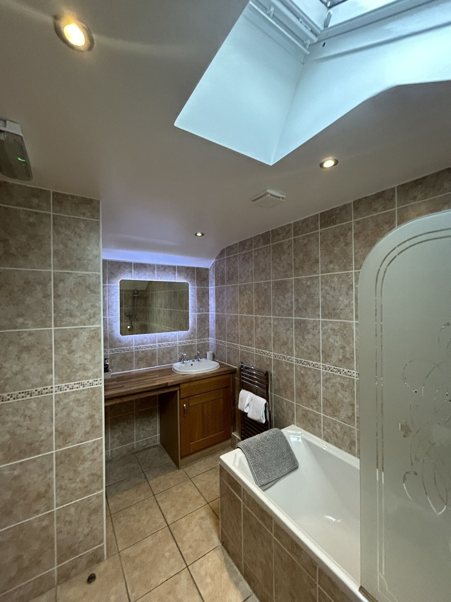 Un baño moderno con tragaluz, una bañera grande, un tocador con espejo y una zona de ducha.
