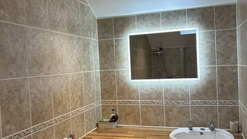 A bathroom with a wooden vanity, a sink, a mirror, and a shower.