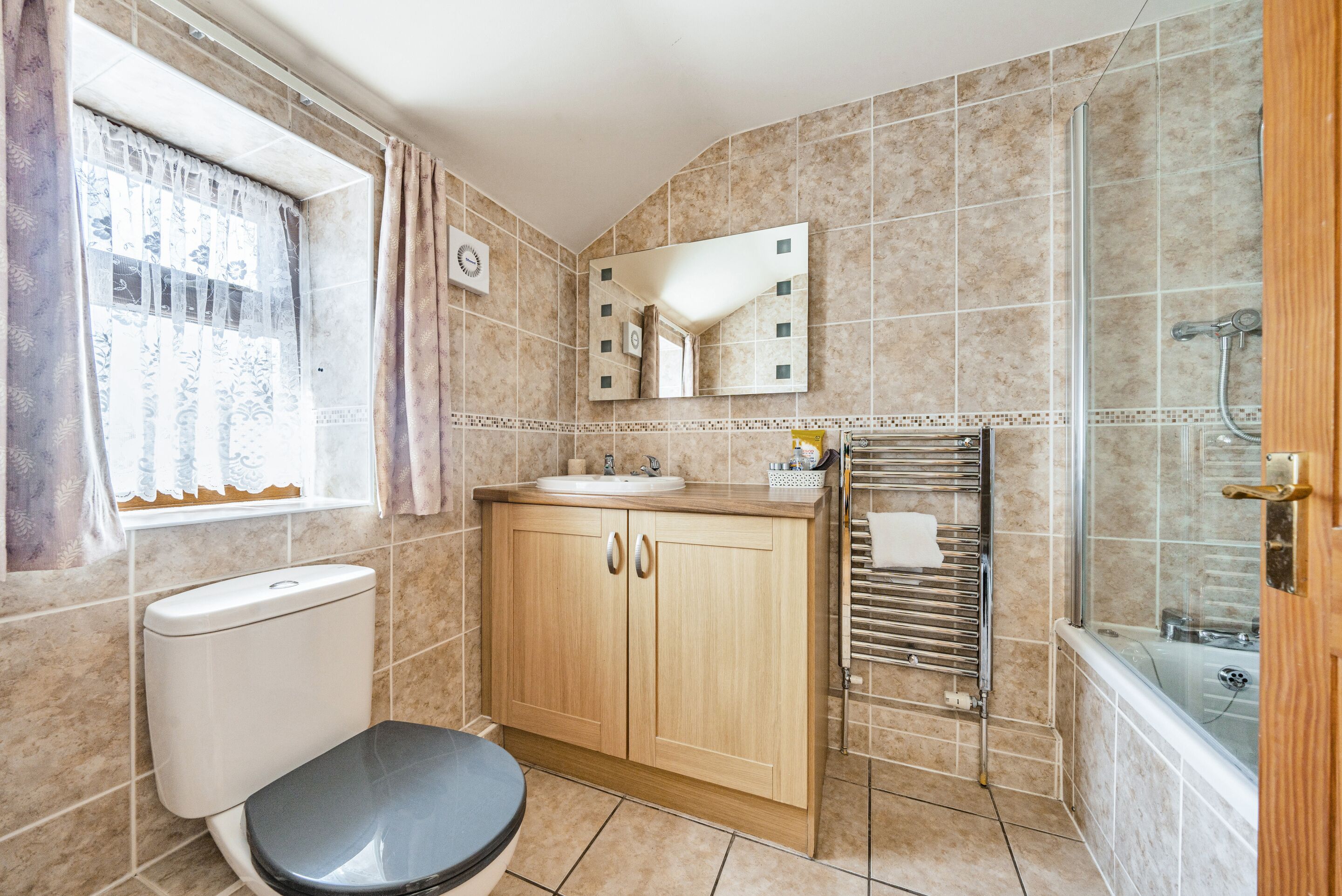 Une salle de bain comprenant des toilettes, un lavabo, un miroir, une douche et une fenêtre avec des rideaux.