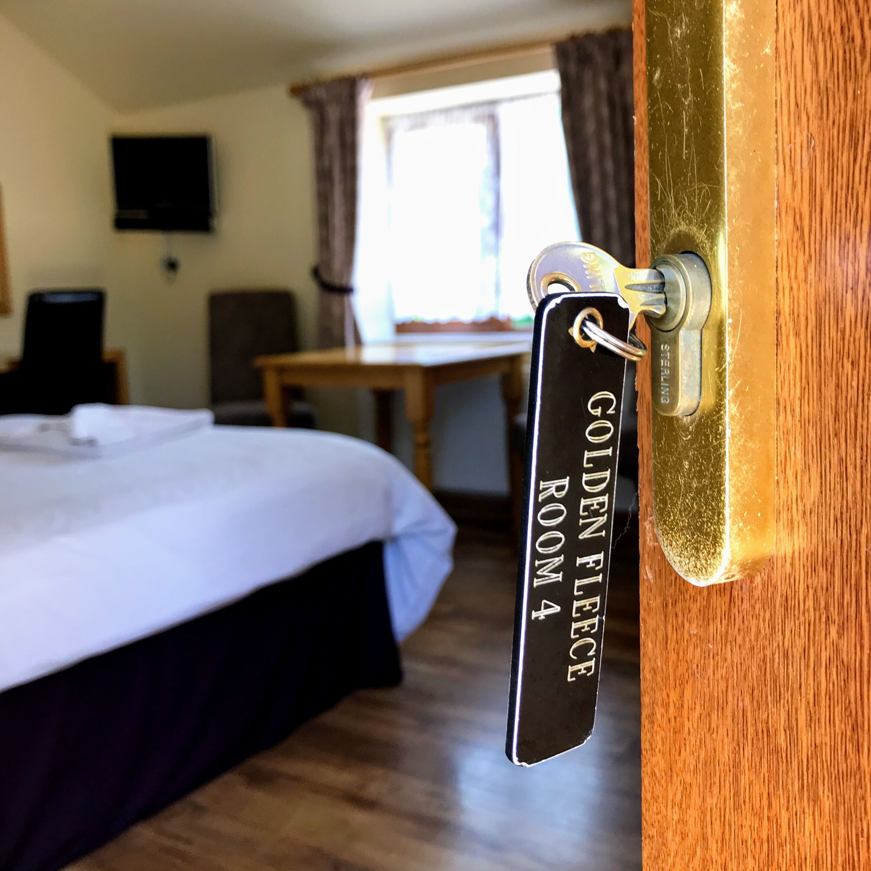 A hotel room with a bed, a desk, and a television on the wall. A sign on the door reads "Golden Fleece Room 4".