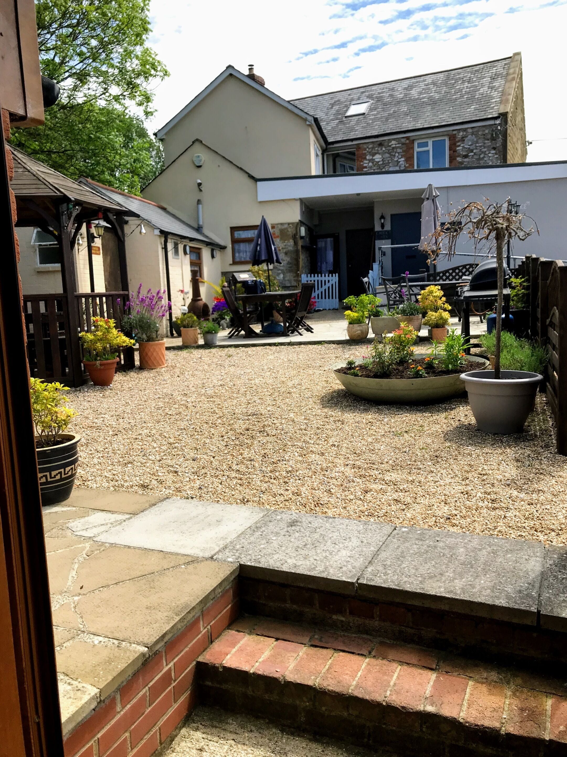 A courtyard with a gravel ground, potted plants, a barbecue area, and a dining table with chairs.