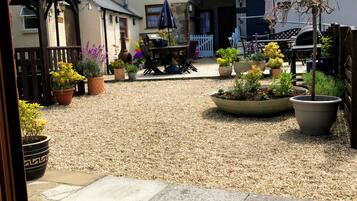 A courtyard with a gravel ground, potted plants, a barbecue area, and a dining table with chairs.