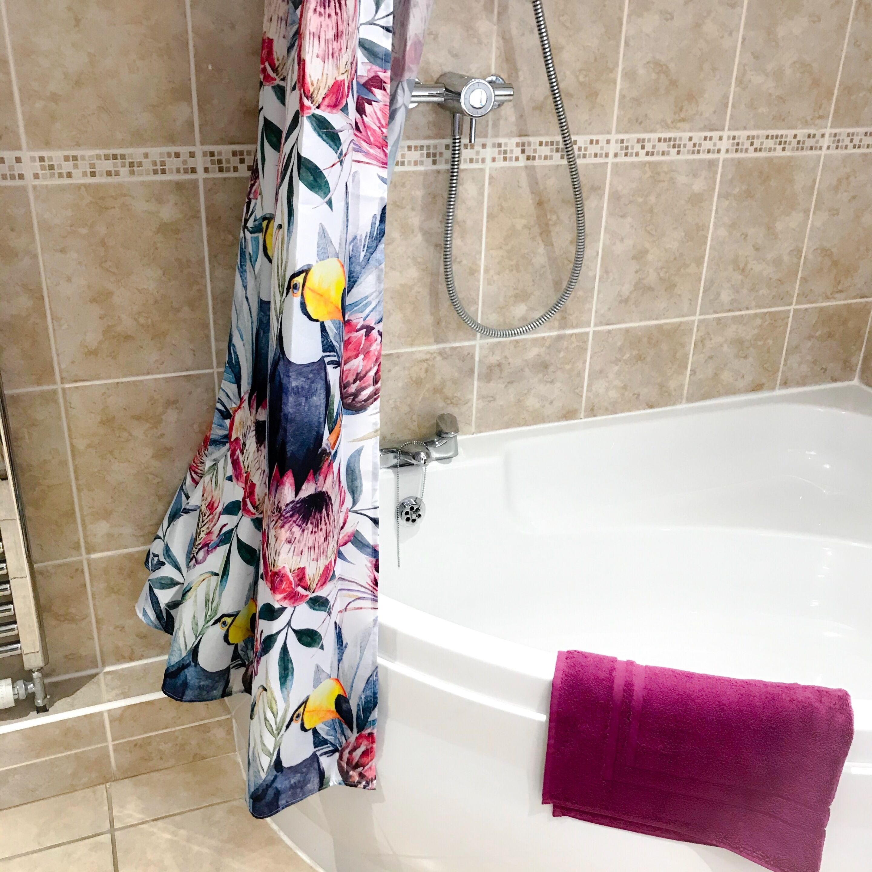 A bathroom with a bathtub, a shower head, and a floral shower curtain.