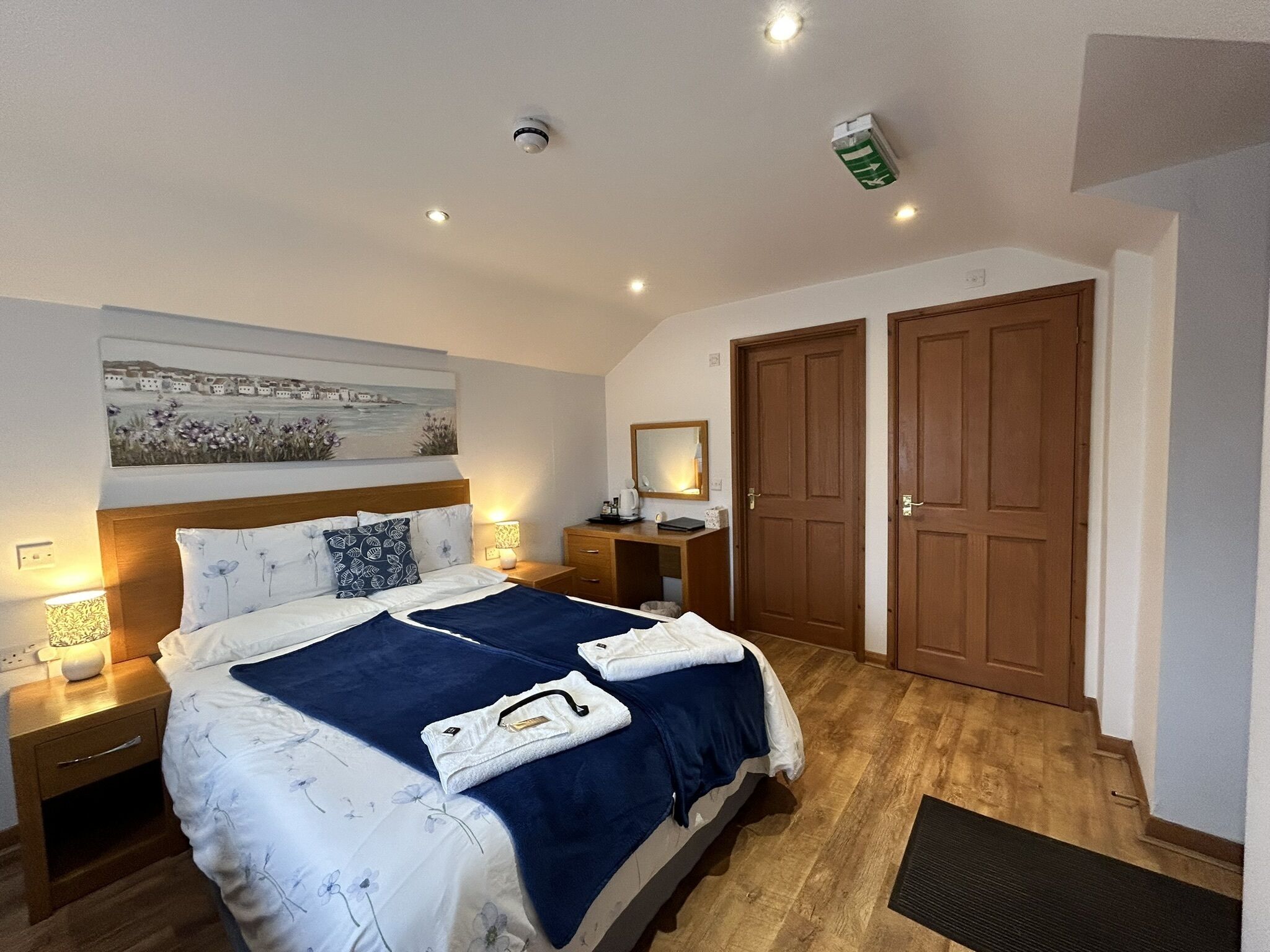 Un dormitorio con cama, mesitas de noche, un espejo y una puerta.
