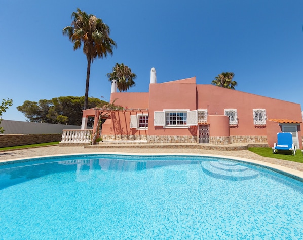 A swimming pool with a clear blue water surface, surrounded by a red building with white windows and a stone base.