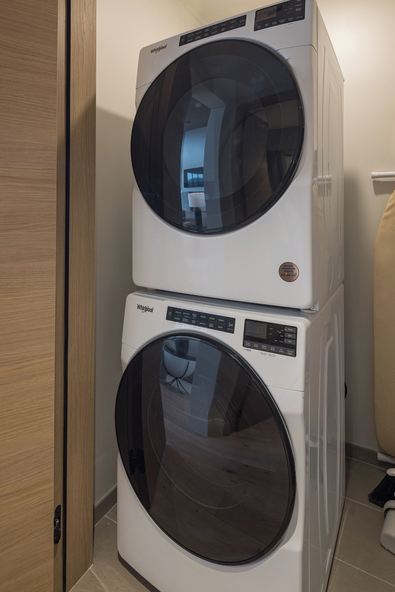 A stacked washer and dryer unit in a room with a wooden door and tiled floor.