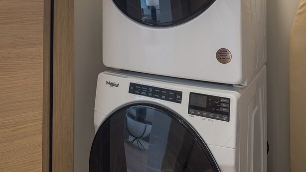A stacked washer and dryer unit in a room with a wooden door and tiled floor.