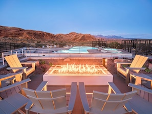 A pool area with lounge chairs, a fire pit, and a view of mountains. - Lionsback Resort (Moab)